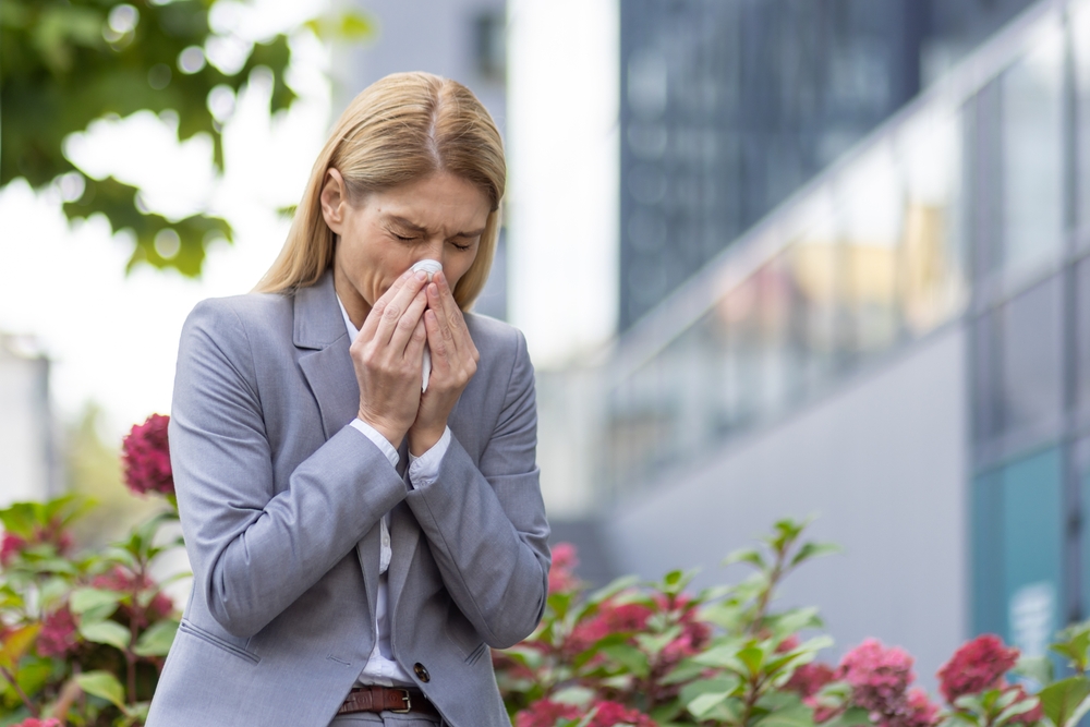 Woman in a business suit sneezing outdoors